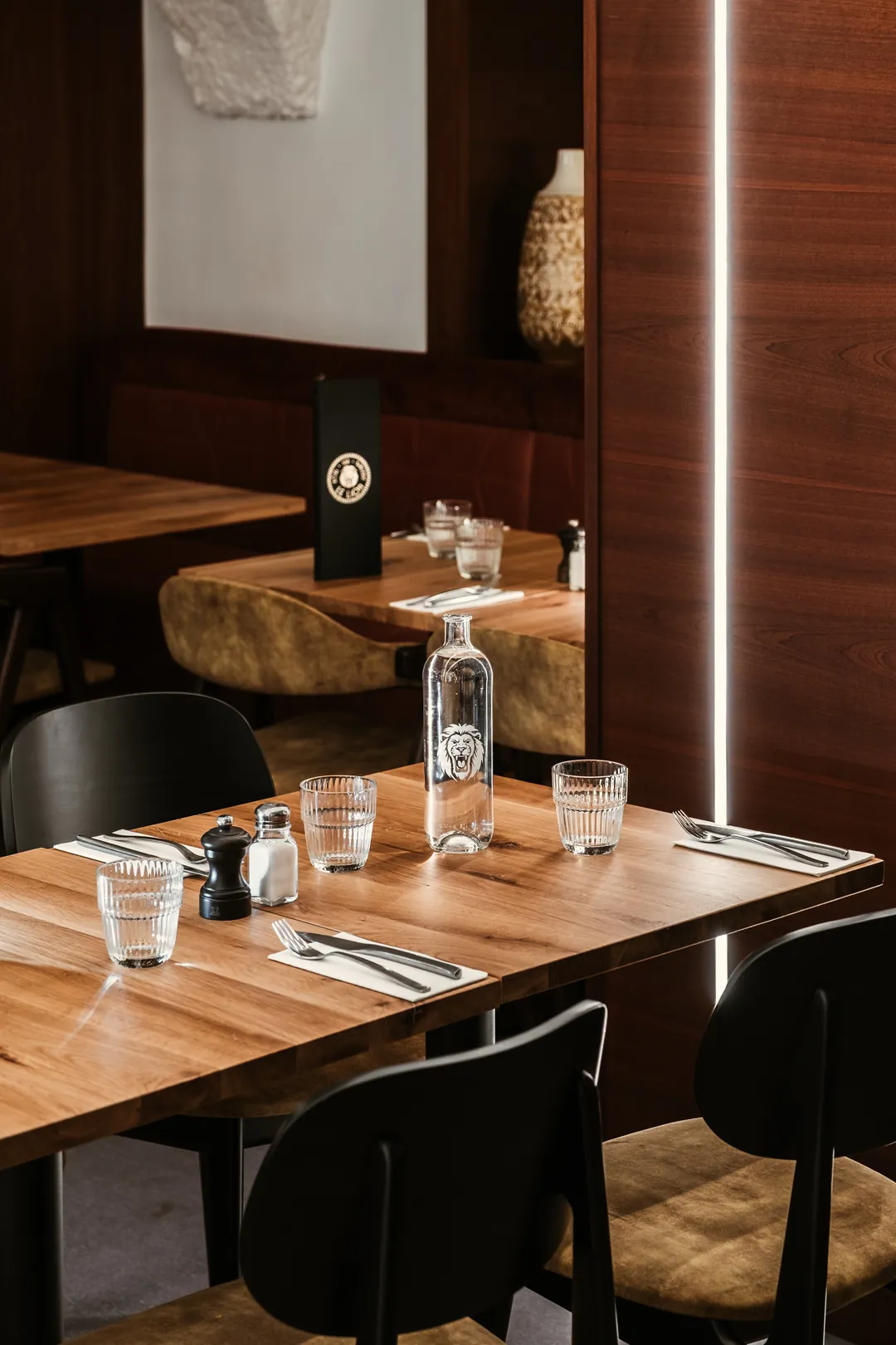 Salle du restaurant Le Lion : table en bois, carafe gravée au lion, verres
