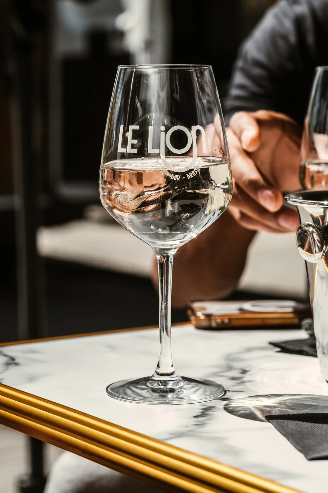 Verre à vin gravé du logo Le Lion sur une table en marbre cerclée de laiton
