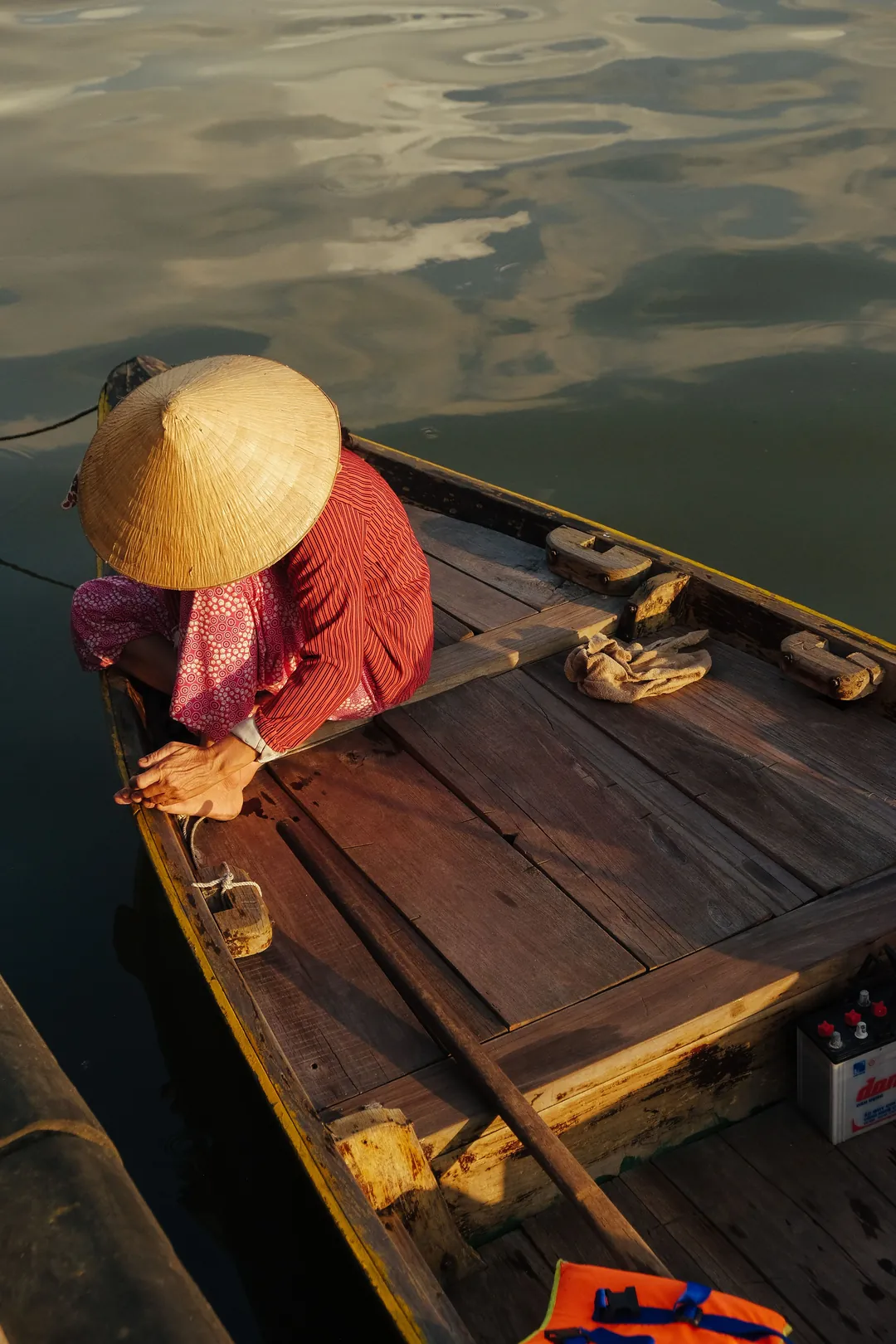 Femme au chapeau conique assise à la proue d’une barque en bois